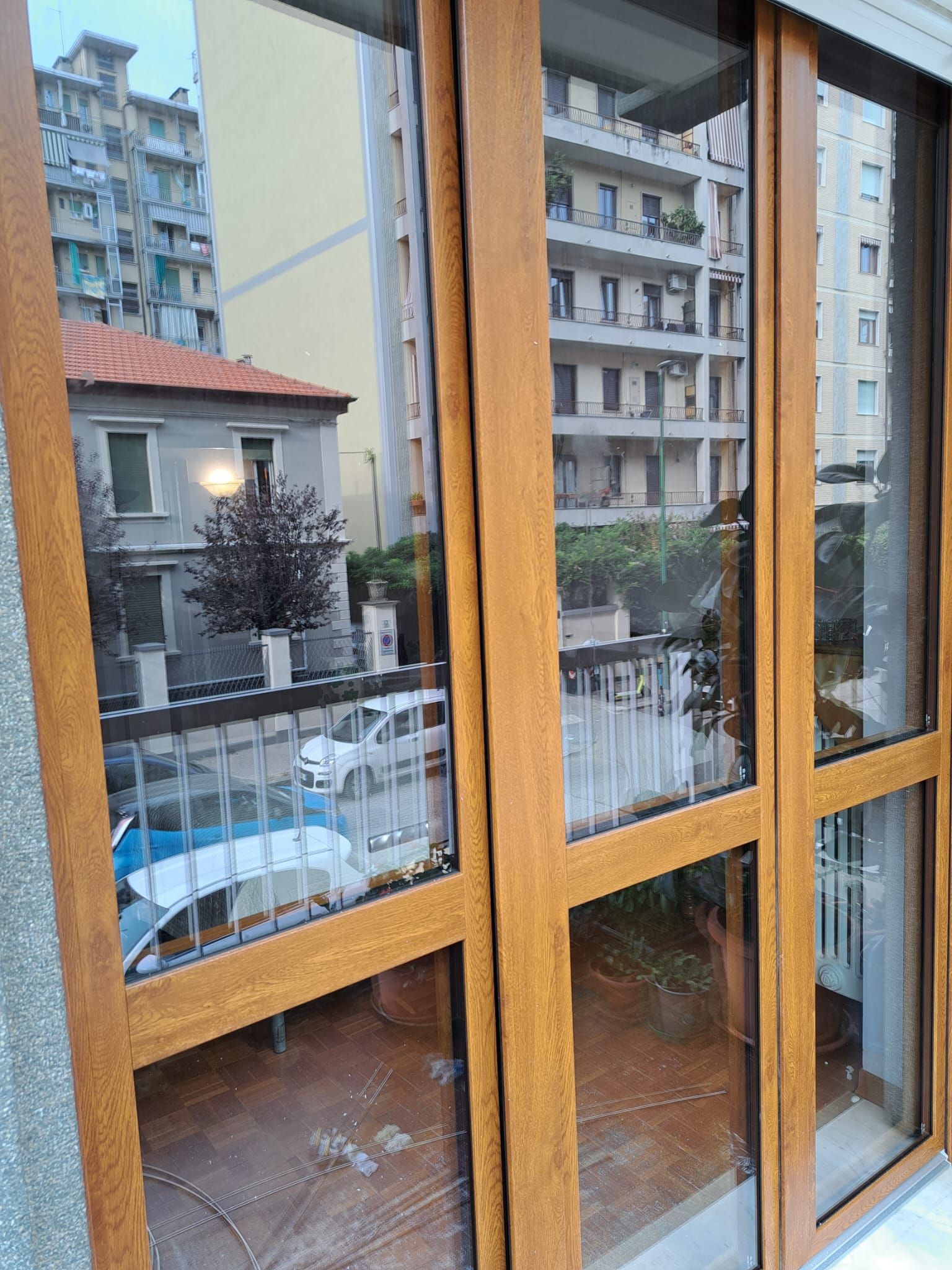 Vista attraverso le porte in vetro con cornice marrone di edifici urbani, balconi e un'auto.