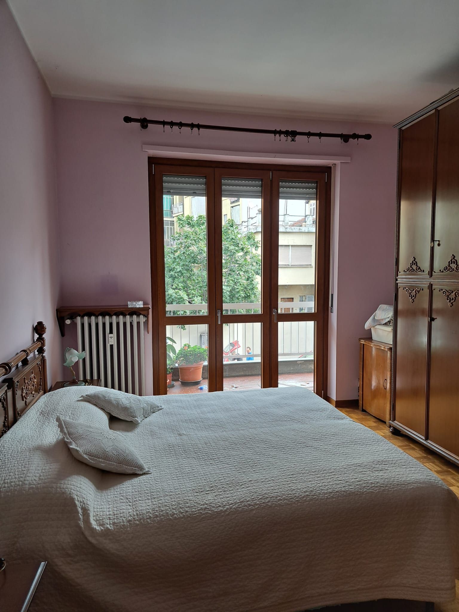 Camera da letto con letto, porte che danno sul balcone, pareti rosa e armadio in legno.