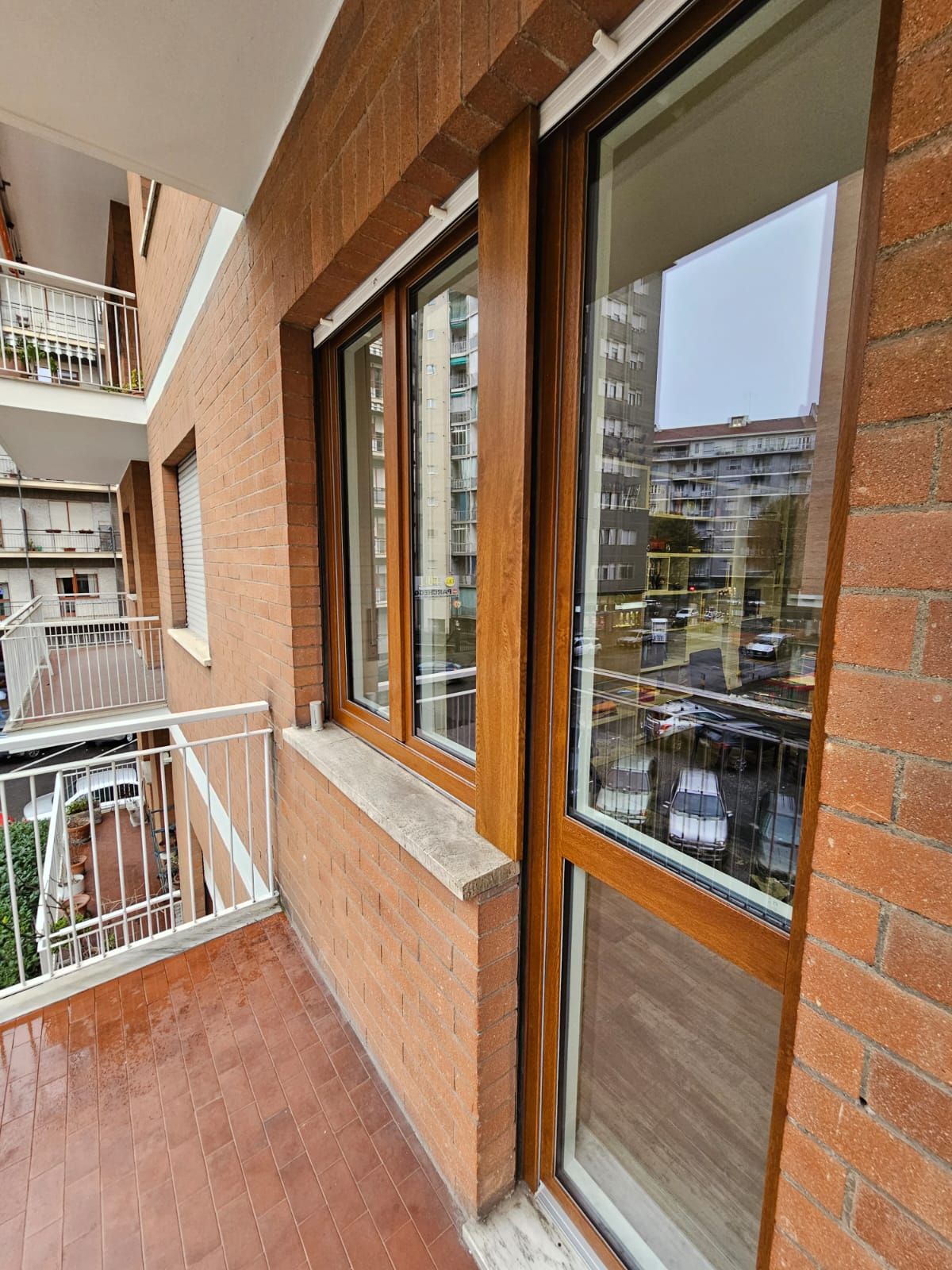 Balcone con pareti in mattoni, infissi in legno e vista sugli edifici della città.