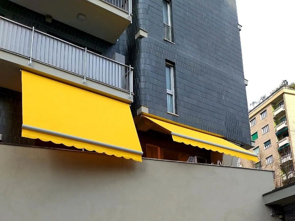 Tende gialle su un edificio con facciata grigia, che forniscono ombra.
