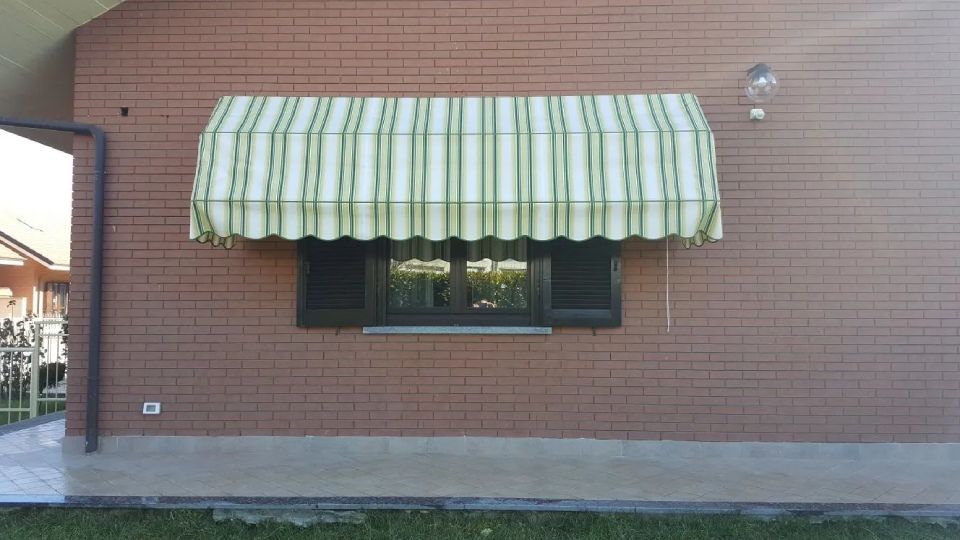 Una finestra con tenda da sole, su un edificio in mattoni. La tenda è a strisce verdi e bianche.
