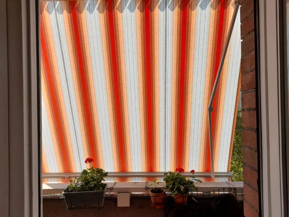 Tenda da sole a strisce arancioni e bianche su un balcone con piante in vaso.