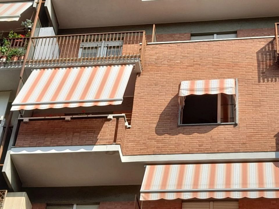 Edificio in mattoni con balconi. Tende a strisce forniscono ombra.