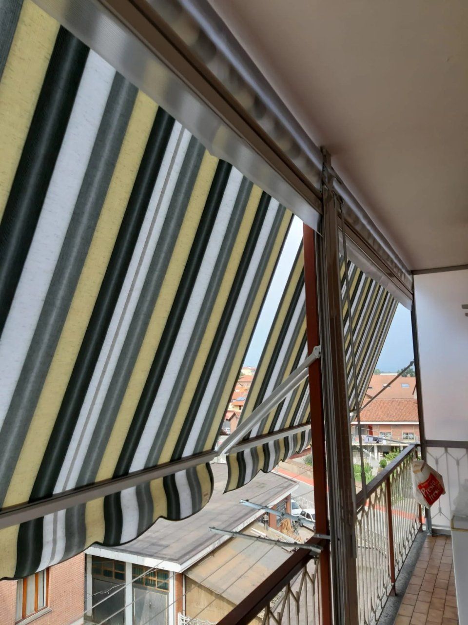 Tenda a strisce su un balcone, che ripara la vista degli edifici e del cielo.