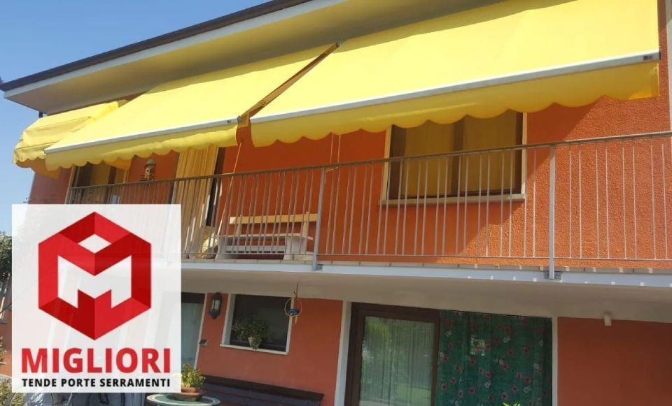 Tenda da sole gialla sul balcone di un edificio; esterno in stucco rosso; il logo