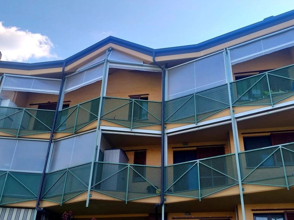 Edificio residenziale a più piani con balconi, ringhiere verdi e tende trasparenti.