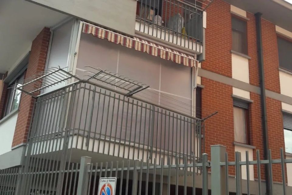 Balcone di un edificio con facciata esterna in mattoni marroni e tenda a strisce.