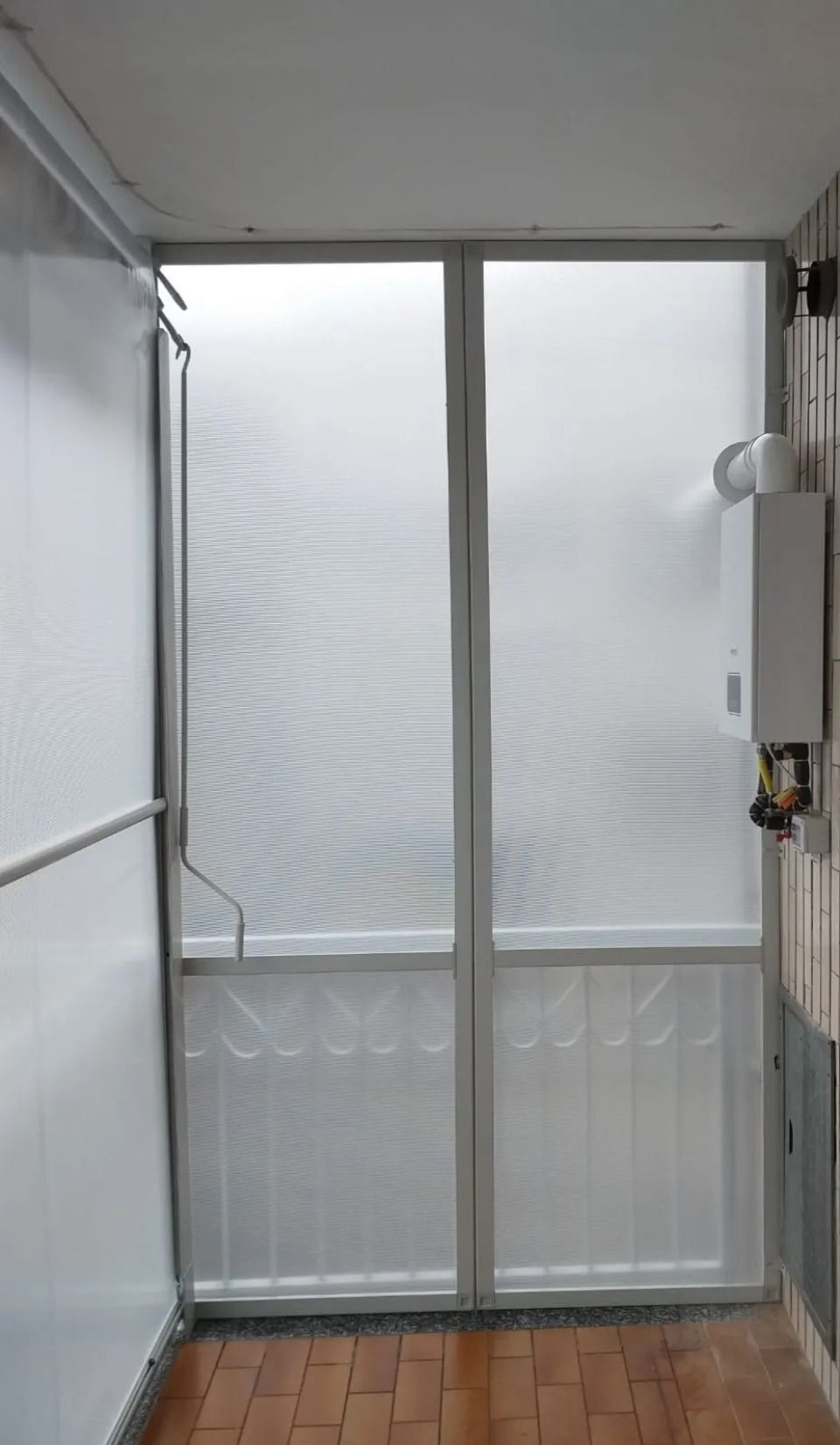 Una porta bianca con pannelli in vetro testurizzato. Uno scaldabagno è montato sulla parete di destra. Pavimento in legno.