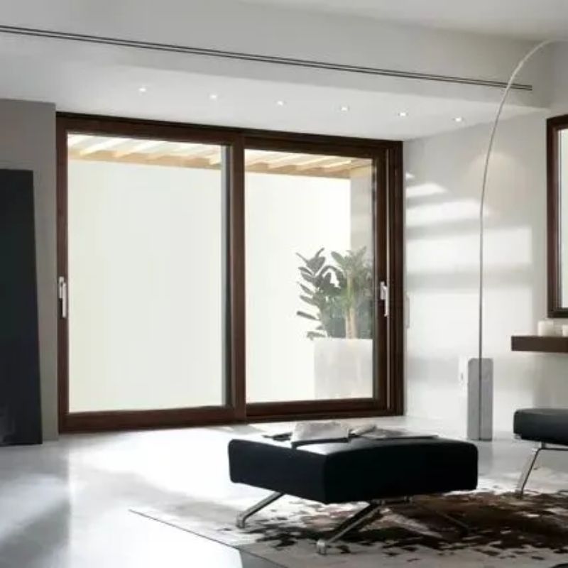 Soggiorno moderno con ampie porte scorrevoli in vetro, cornici marroni e vista su un'area esterna luminosa.