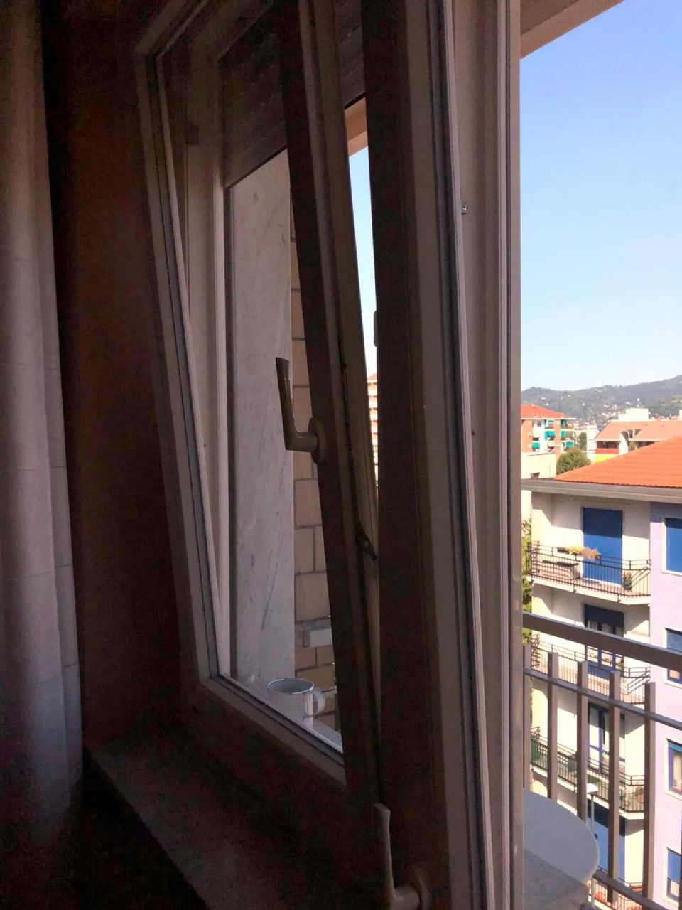 Finestra aperta con vetro inclinato. Vista esterna degli edifici e del cielo azzurro.