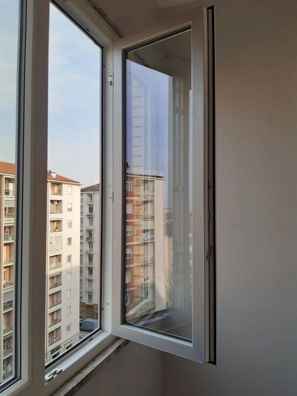 Finestra bianca aperta con vista sugli edifici della città in una giornata di sole.