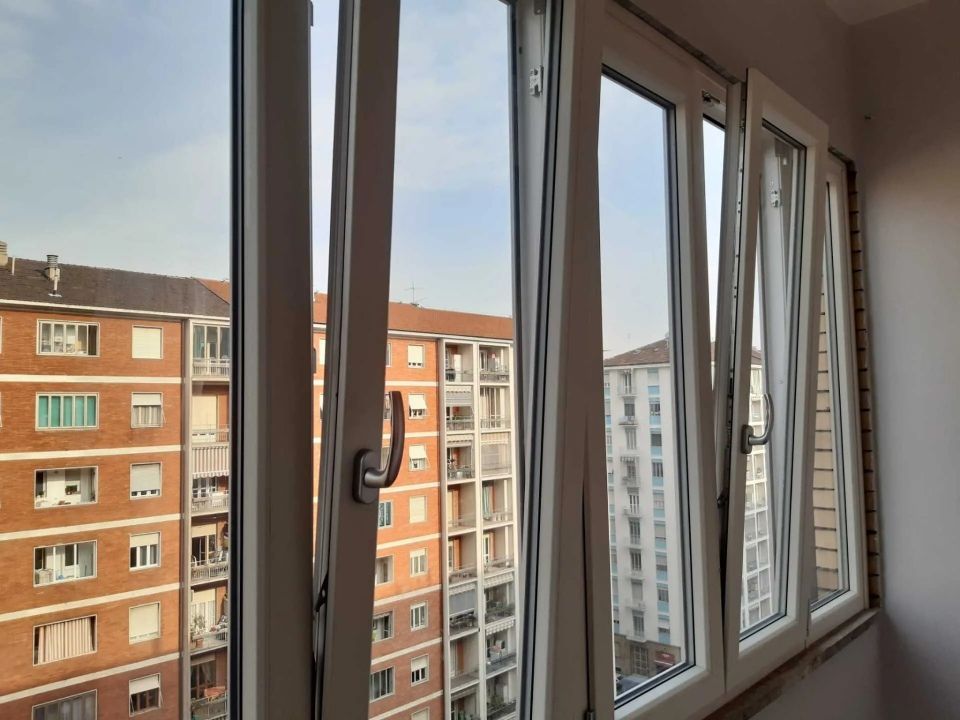 Aprite le finestre bianche con vista sui palazzi in mattoni che si stagliano contro il cielo azzurro.