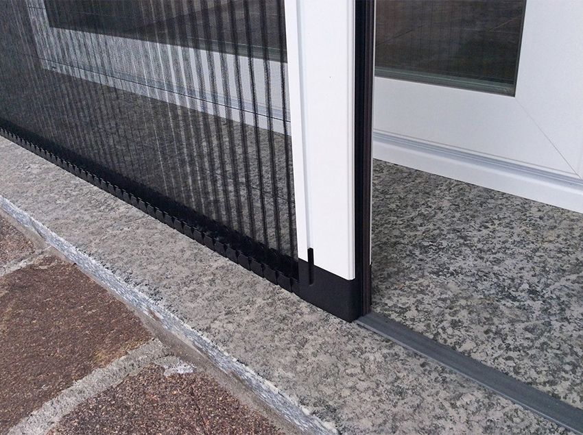 Porta a zanzariera nera retrattile installata su una soglia in pietra.