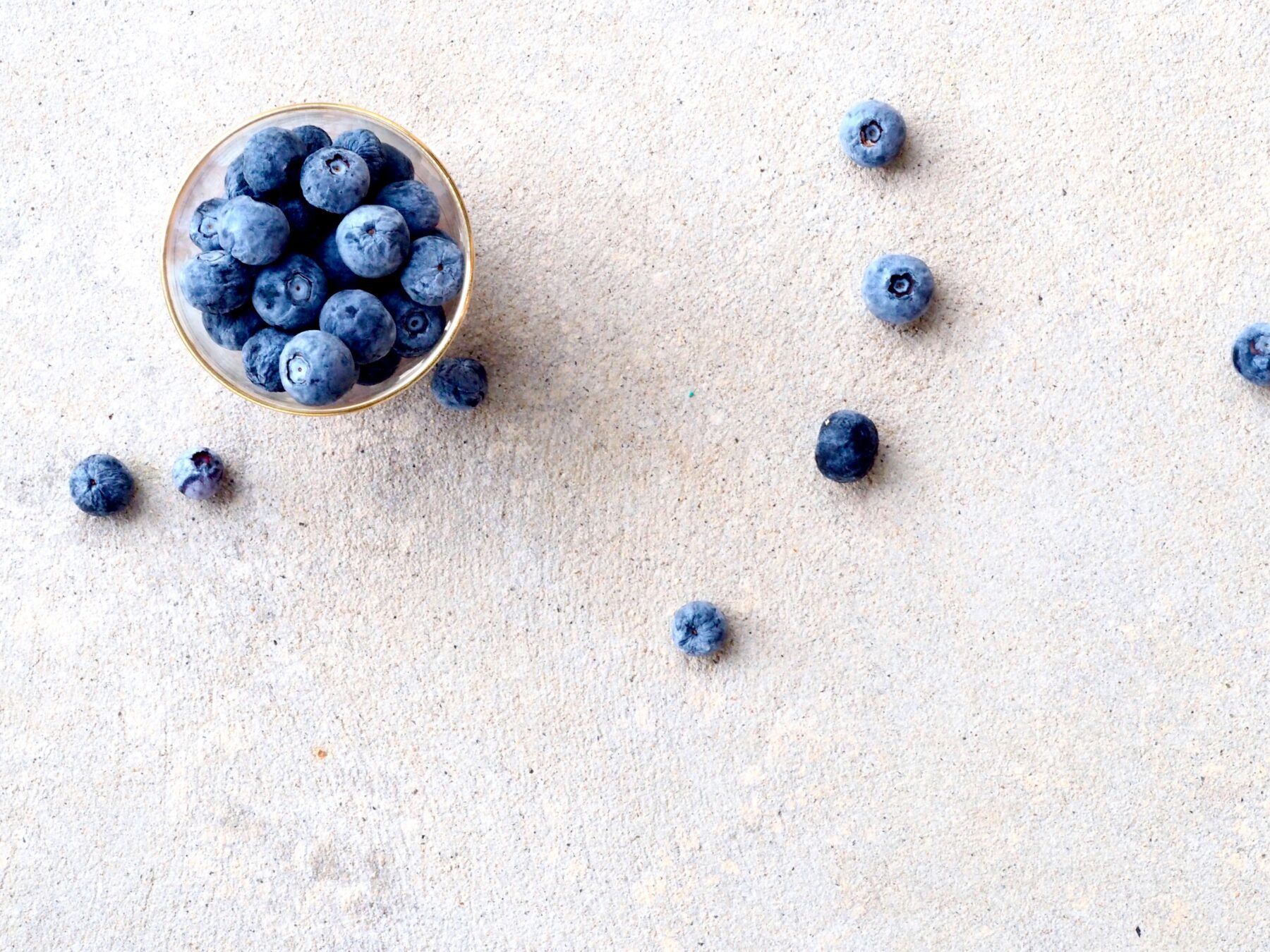Small bowl of blueberries with some scattered on table