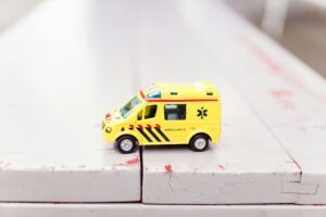 Toy yellow ambulance van driving across white porch boards.