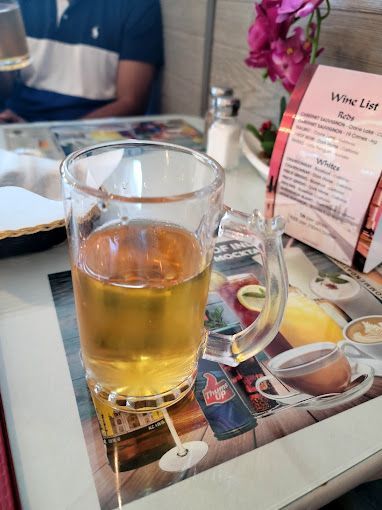 Beer in a glass mug on a restaurant table, near a wine list and a person wearing a blue shirt.