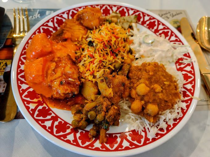 A plate with various Indian dishes: chicken tikka masala, biryani rice, and vegetables.