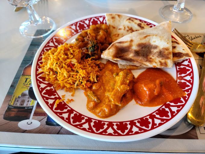Plate of Indian food: rice, curry, naan, and sauce on a red-rimmed plate.