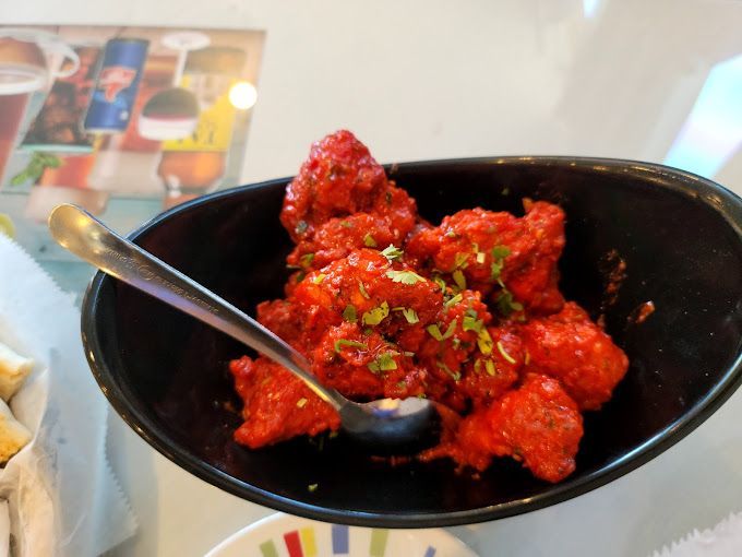 Red-sauce covered cauliflower in a black bowl with a spoon. Some green herbs sprinkled on top.