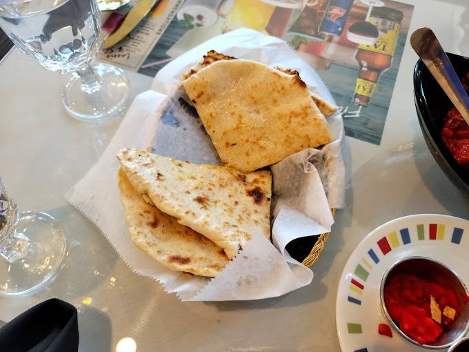 Basket of flatbread with a small dish of red sauce and glass of water on a table.