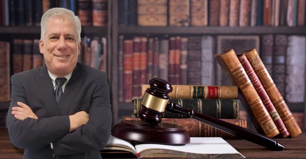 Man in suit with arms crossed, smiling, in a library setting with books and gavel.