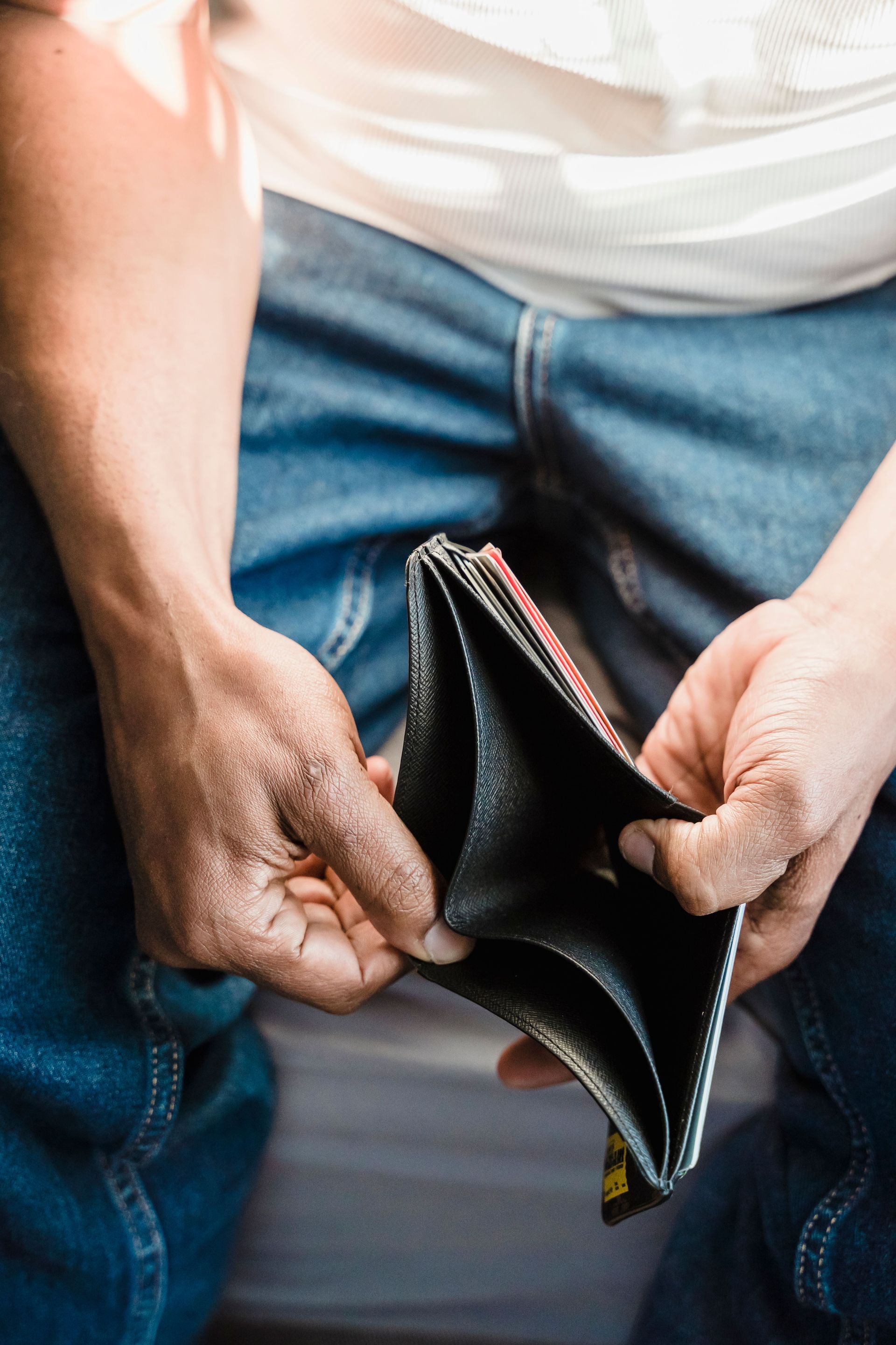 Empty black wallet held open over blue jeans, showing no cash or cards