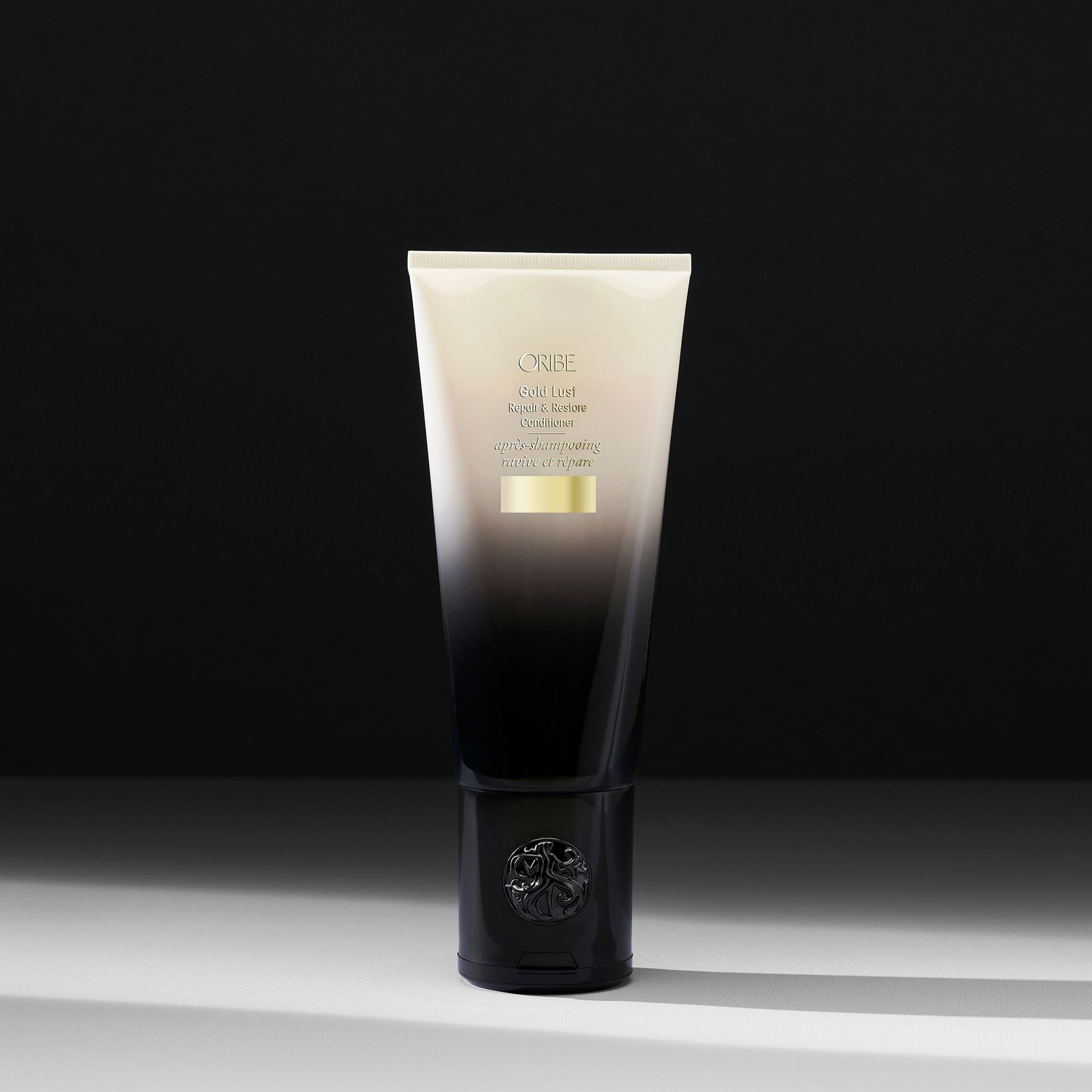 A tube of Oribe Gold Lust Repair & Restore Conditioner transitioning from white at the top to black at the base.
