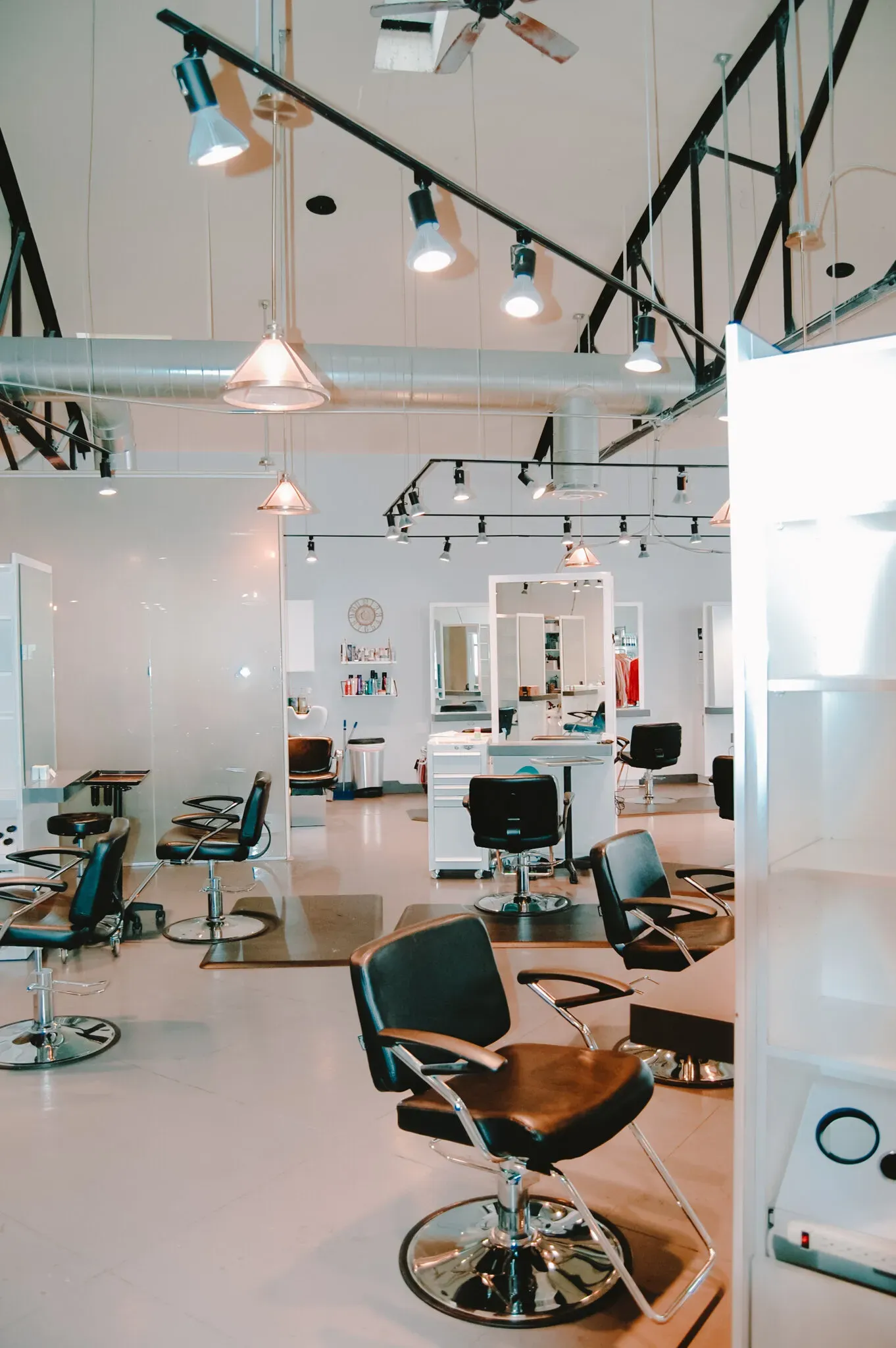 Interior view of a modern, well-lit hair salon with multiple styling chairs, white surfaces, and industrial track lighting.