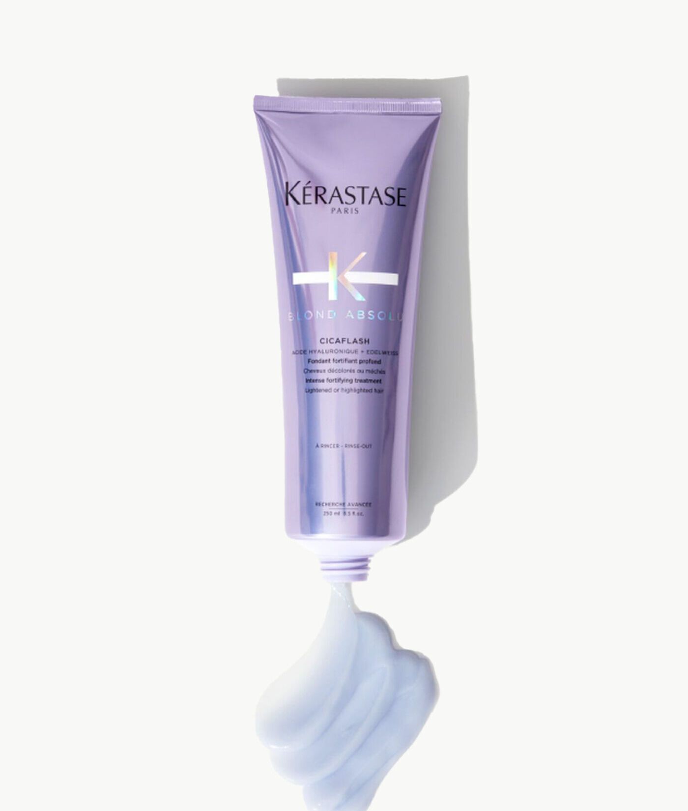A purple tube of Kérastase Cicaplasme hair treatment dispensing a swirl of white cream against a white background.