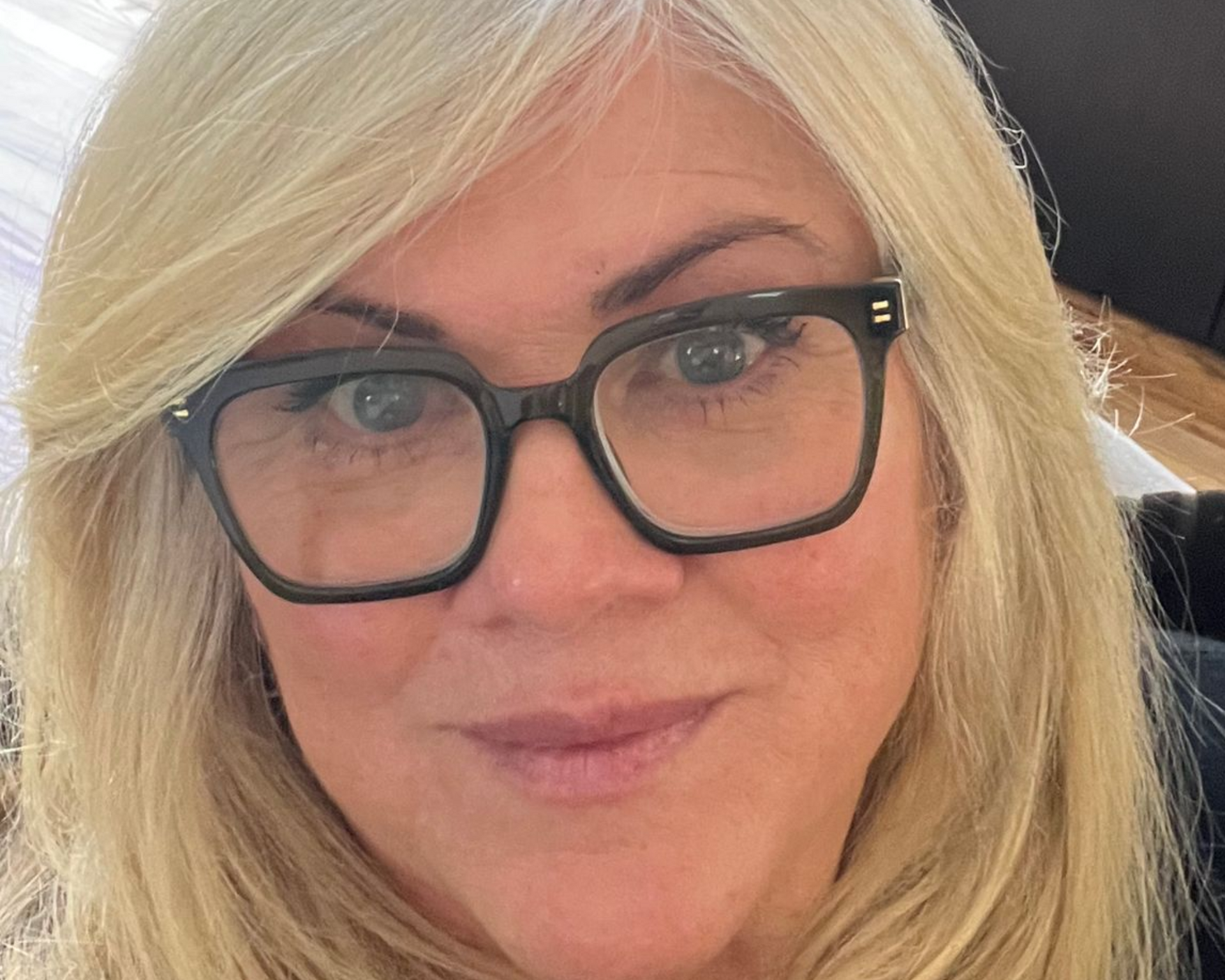 A headshot of a person with blonde hair wearing black-rimmed glasses, looking directly at the camera.