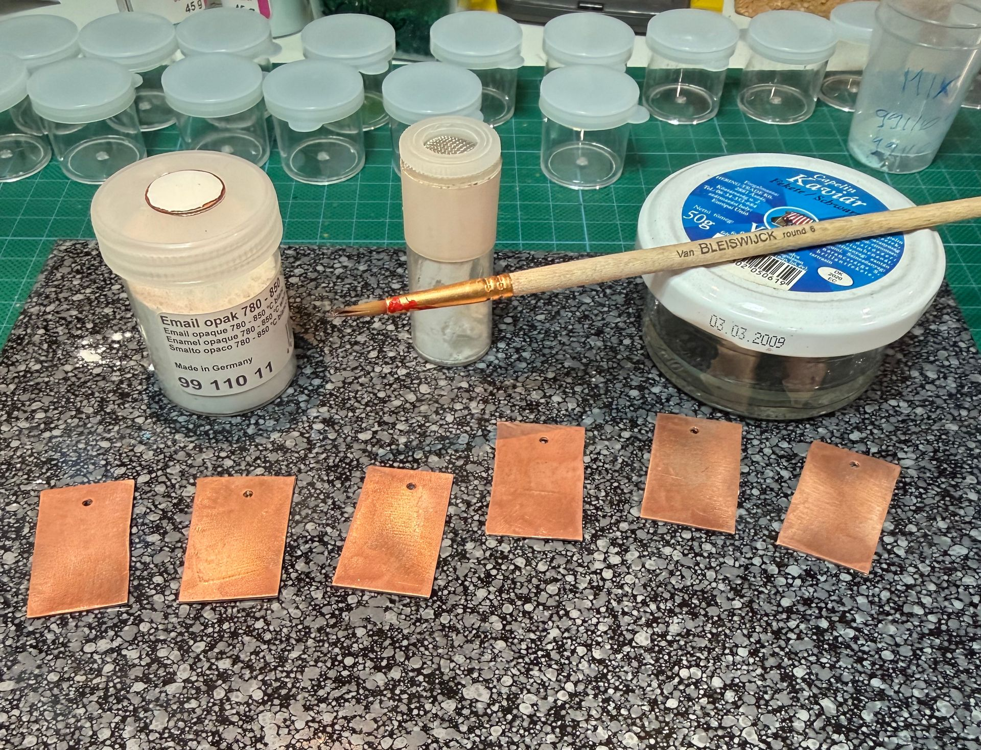 Handgemaakte emaille sieraden in proces – koperen plaatjes, emaille poeders en gereedschap in het atelier van Aynur Sieraden