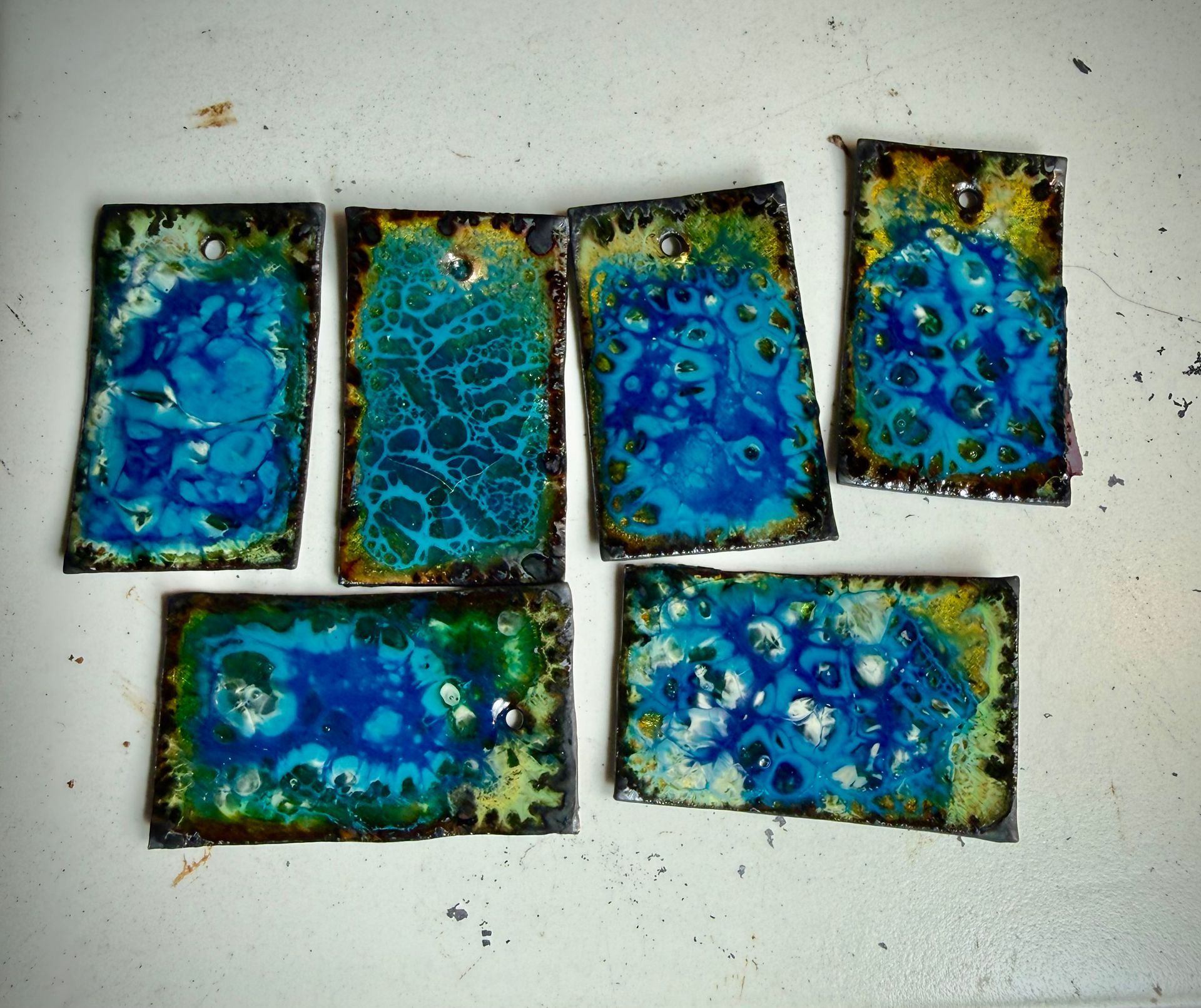 Emaille experiment op koperplaatjes met blauwe en groene patronen – handgemaakt bij Aynur Sieraden