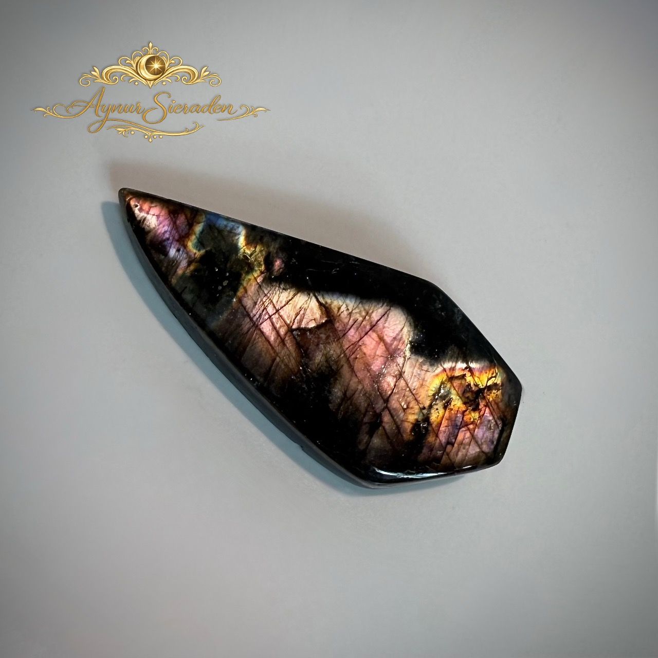 Labradoriet cabochon met roze en gouden glans op lichte achtergrond.