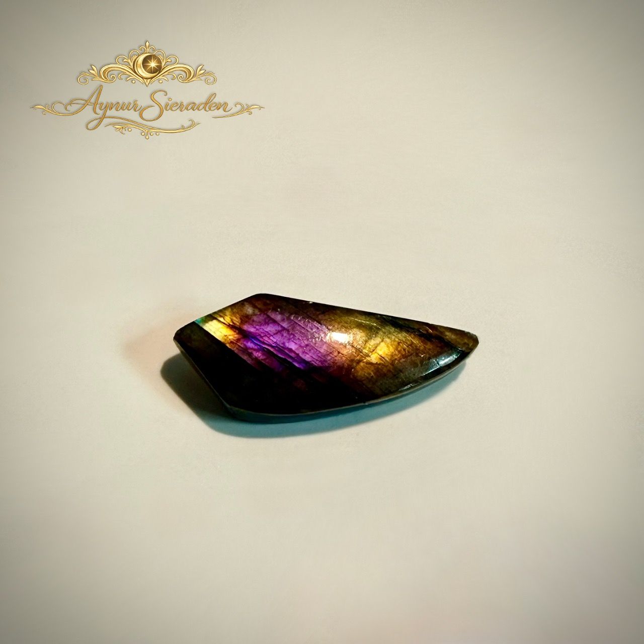 Handgeslepen labradoriet cabochon met paars-gouden kleurenspel voor exclusieve sieraden.