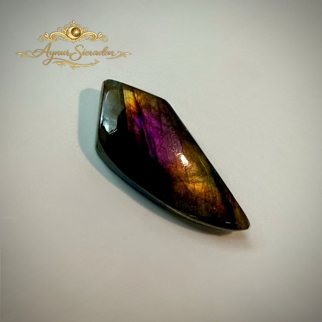 Langwerpige labradoriet cabochon met paarse en gouden labradorescentie.