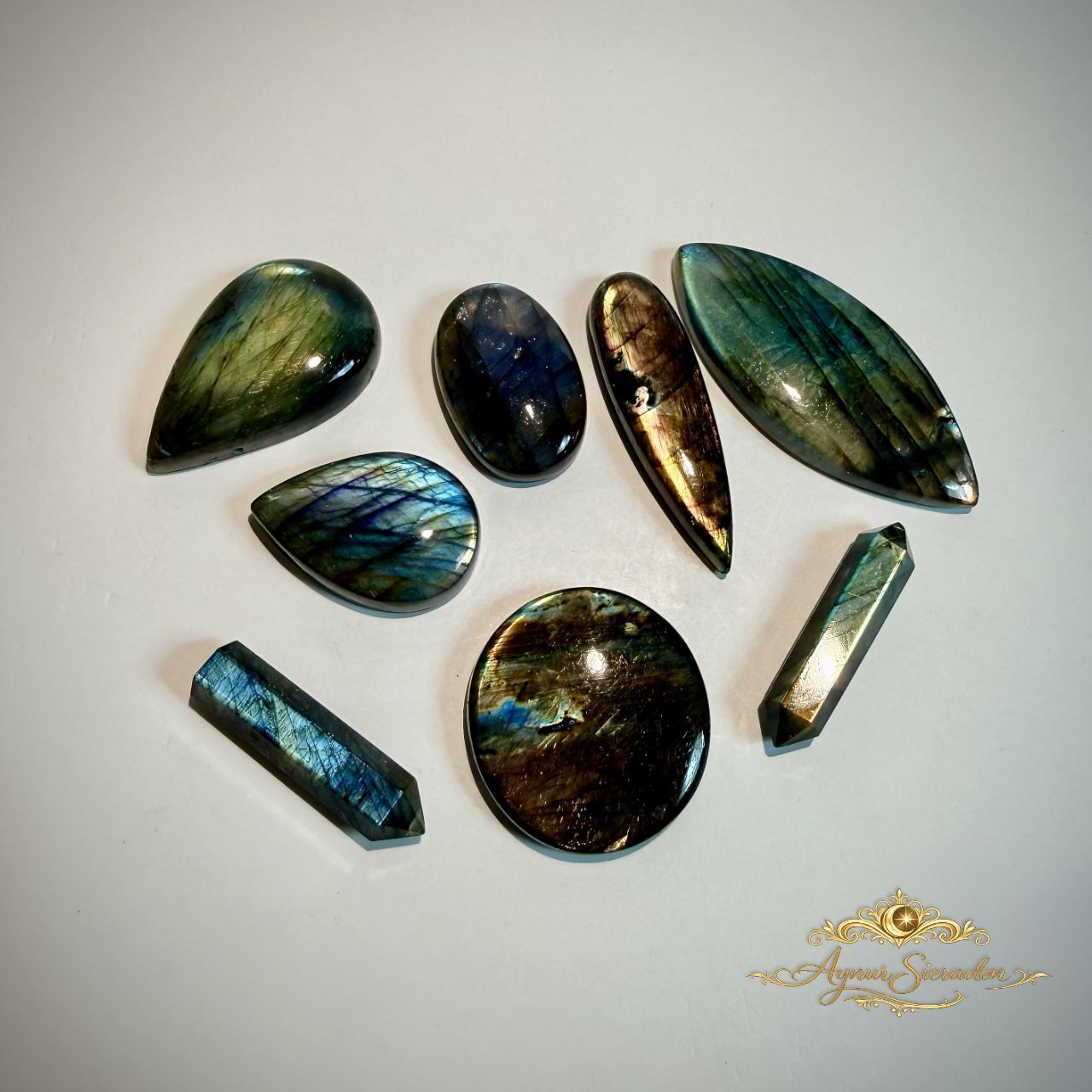 Verschillende labradoriet cabochons met blauwe en groen-gouden glans in diverse vormen op lichte achtergrond.