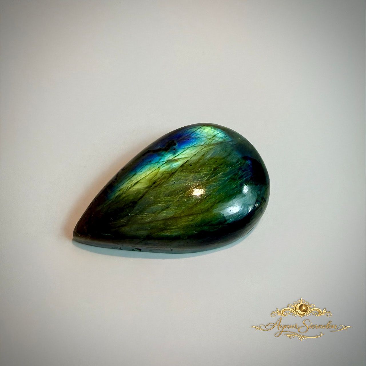 Groen-blauwe labradoriet cabochon in druppelvorm met sterke glans op lichte achtergrond
