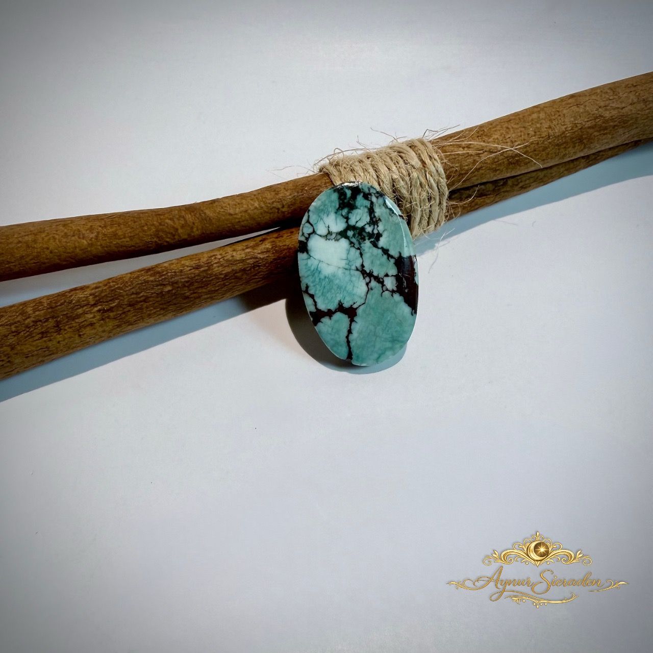 Ovale groenblauwe turkoois cabochon met donkere matrix op houten takken.
