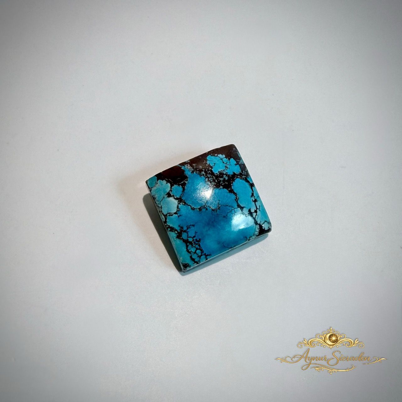 Blauwgroene vierkante turkoois cabochon met zwarte aderstructuur op lichte achtergrond.
