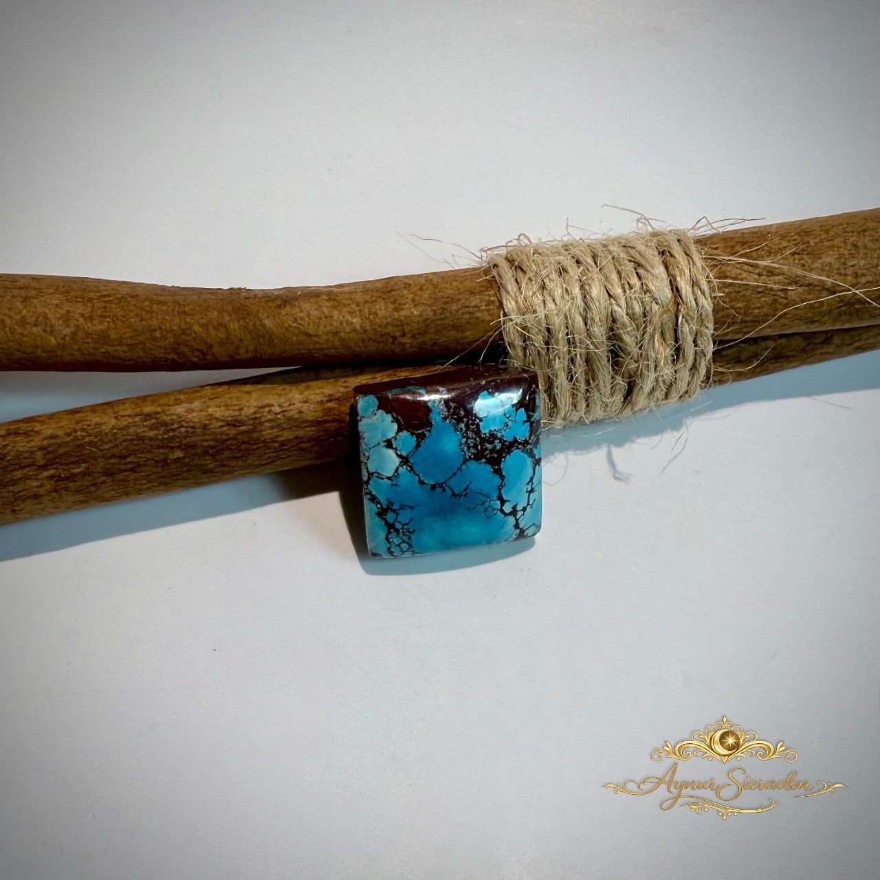 Vierkante blauwe turkoois cabochon met donkere natuurlijke matrix op houten takken.