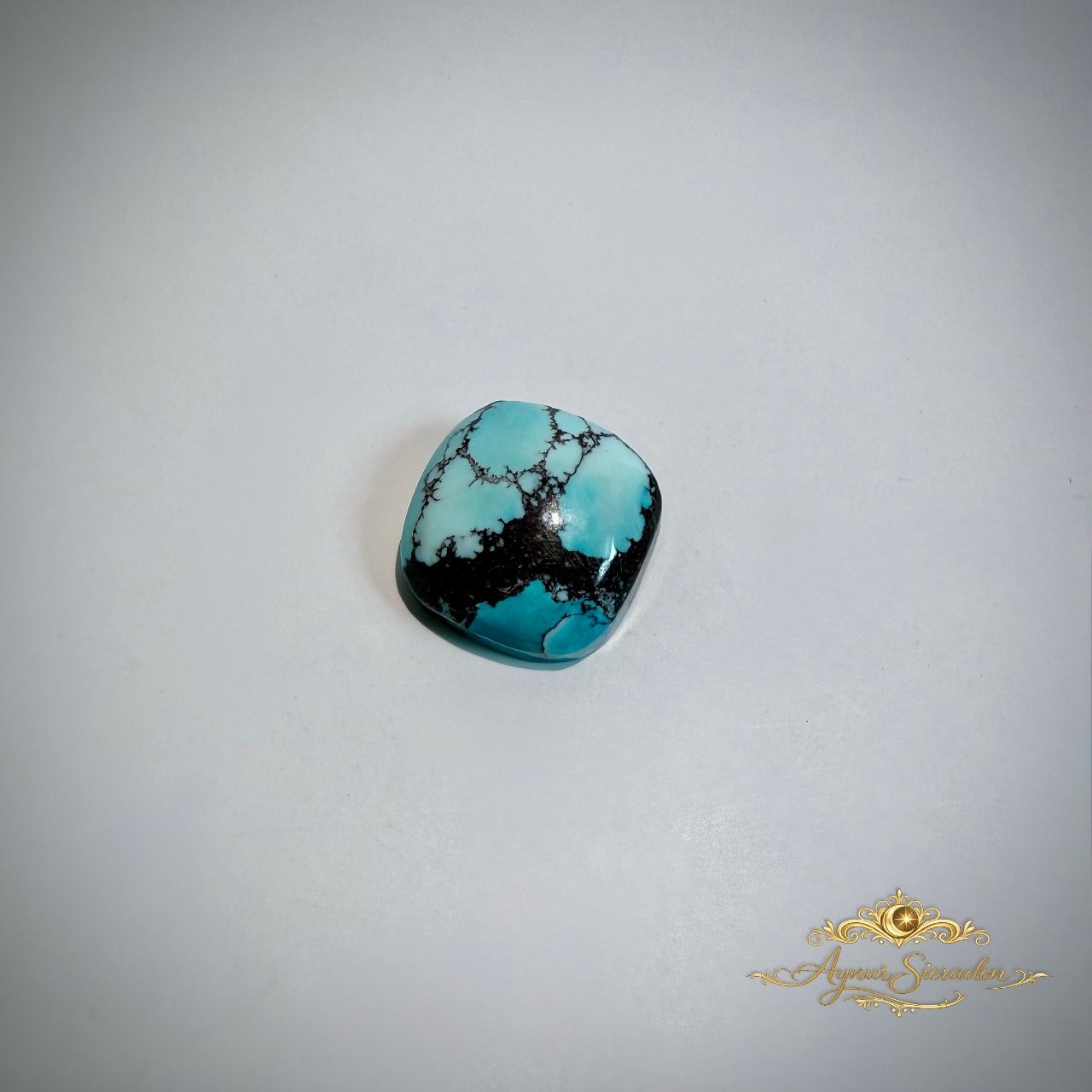 Organisch gevormde blauwe turkoois cabochon met unieke natuurlijke patronen op lichte achtergrond.