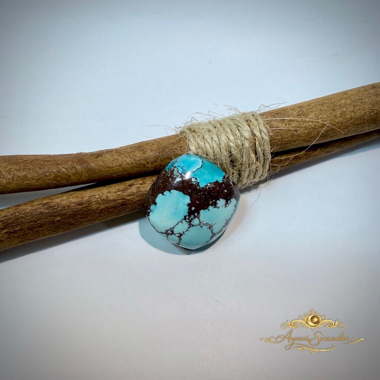 Blauwgroene turkoois cabochon met organische vorm en donkere matrix op houten takken.