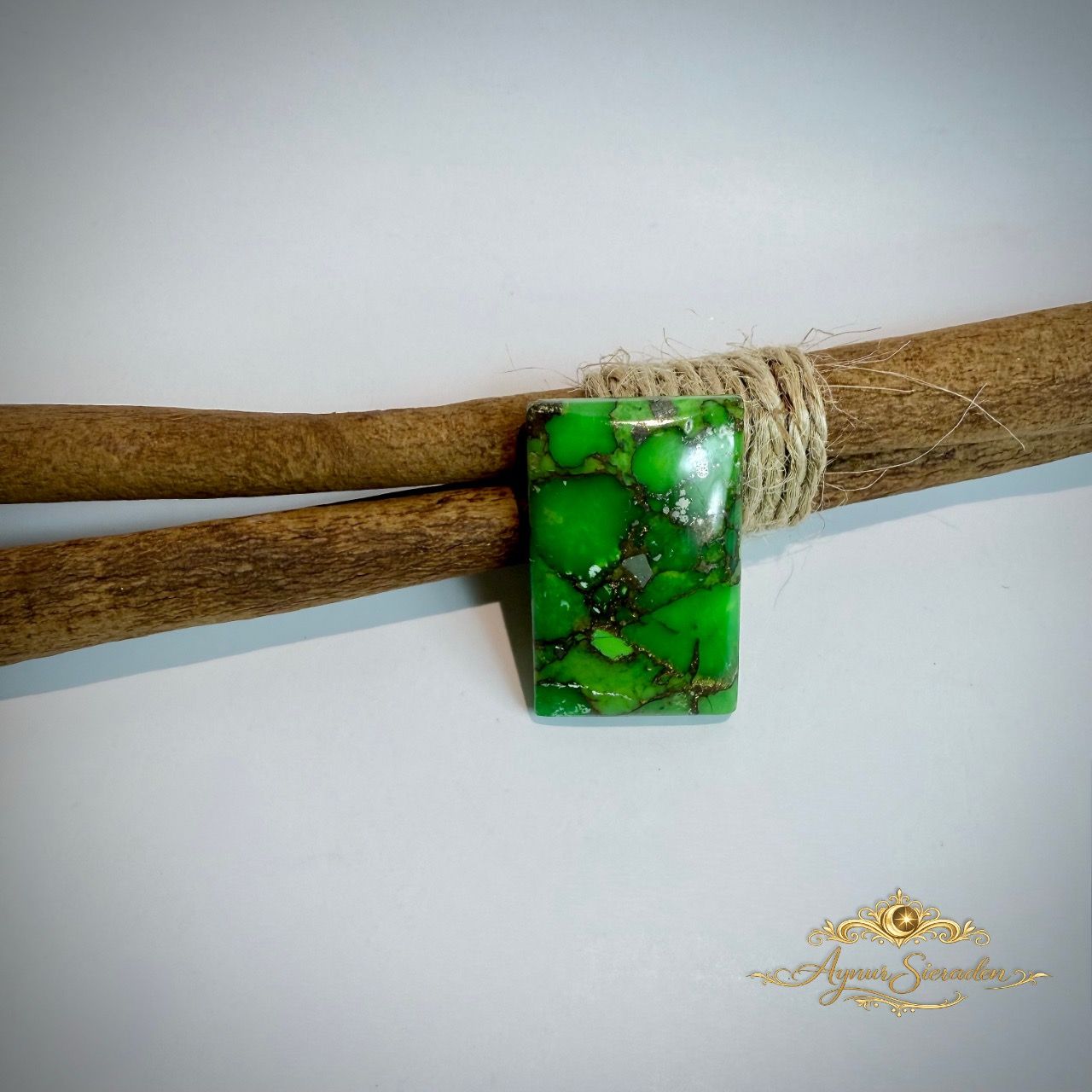 Groene rechthoekige turkoois cabochon met donkere matrix op houten takken.