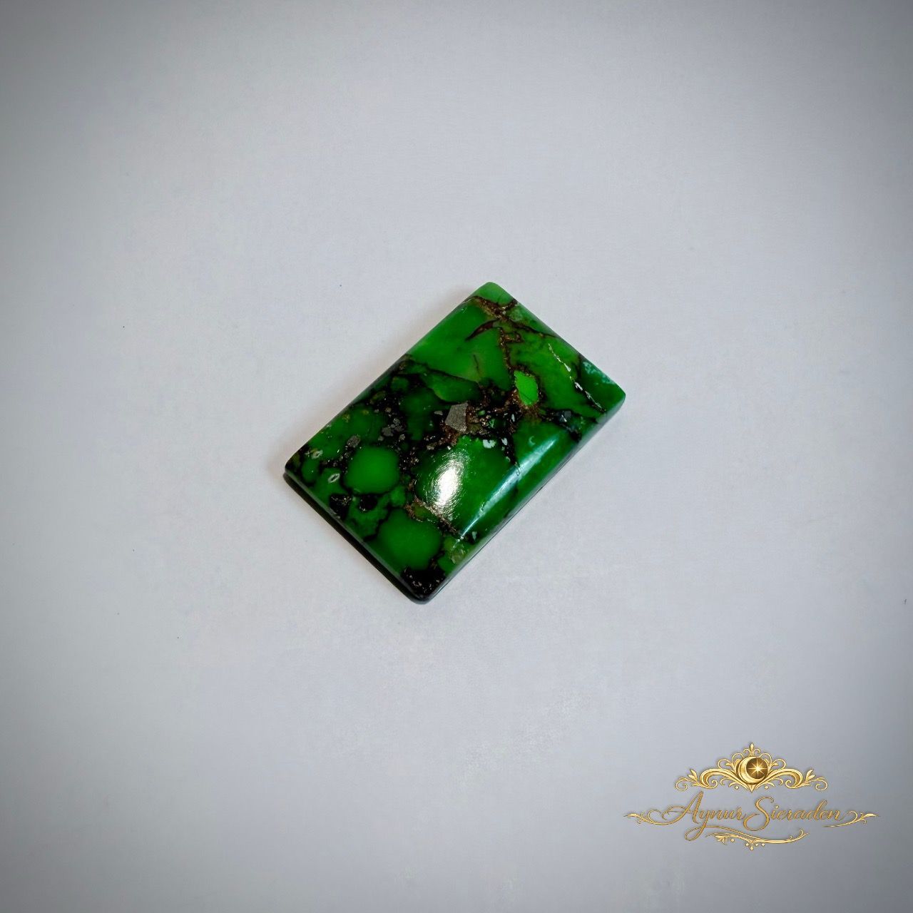 Rechthoekige groene turkoois cabochon met zwarte natuurlijke aderstructuur op lichte achtergrond.