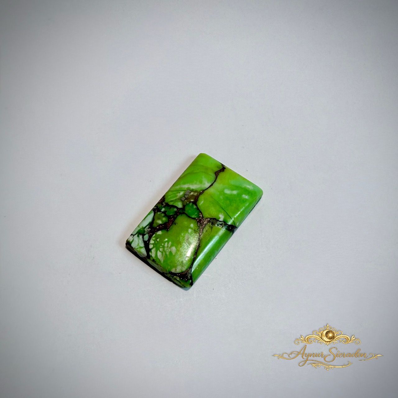 Kleine rechthoekige groene turkoois cabochon met natuurlijke aderstructuur op lichte achtergrond.