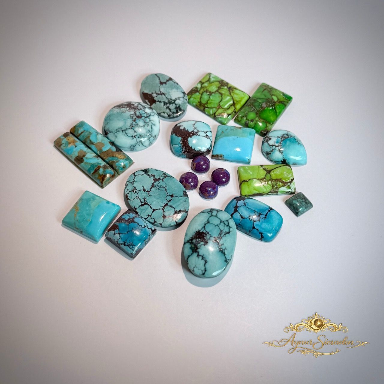 Diverse turquoise en groene edelsteen cabochons en kralen gerangschikt op een witte achtergrond.