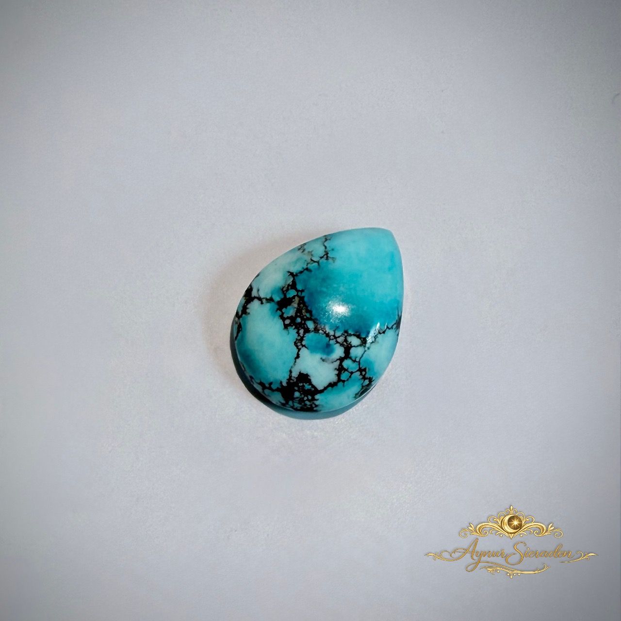 Elegante lichtblauwe turkoois cabochon in druppelvorm op lichte achtergrond.