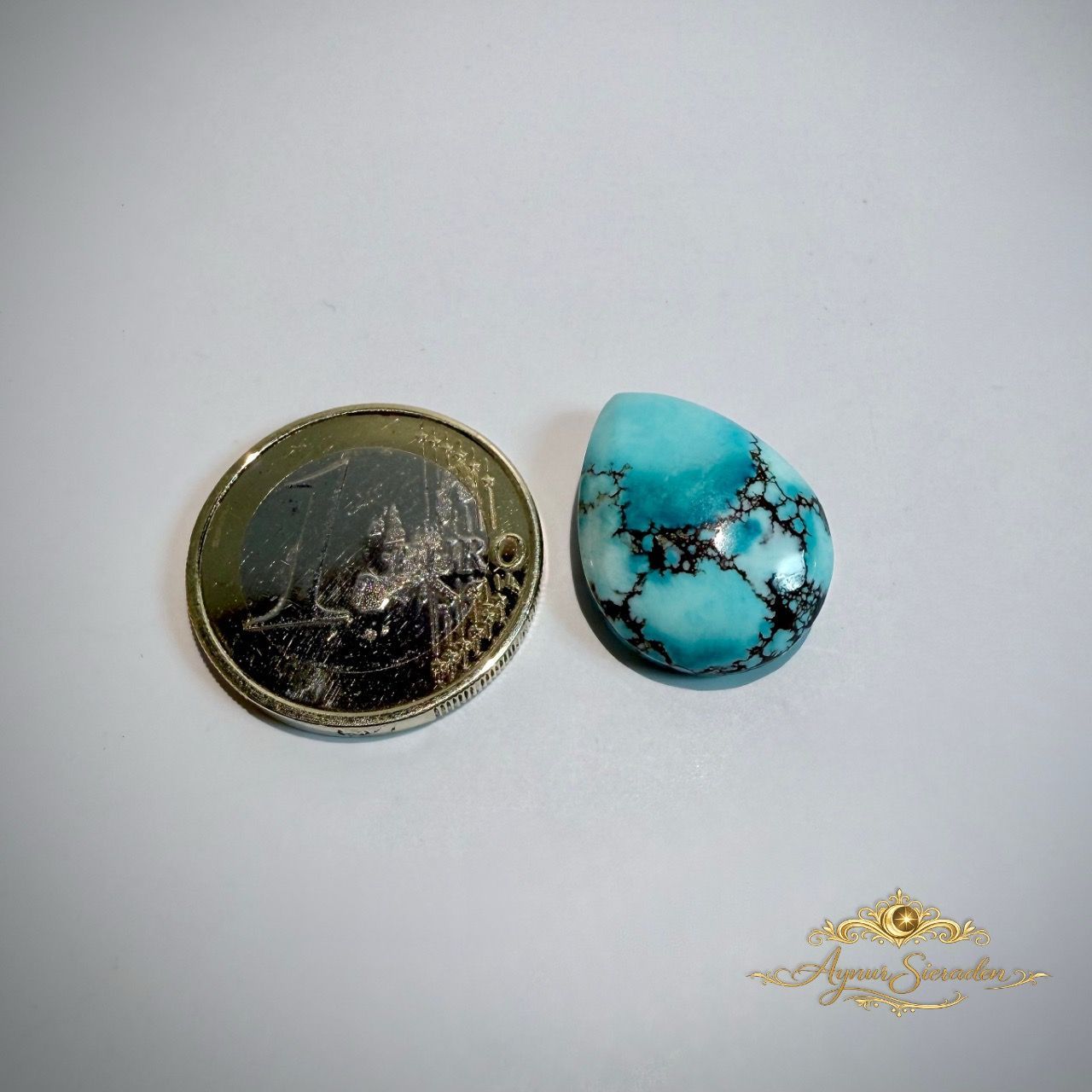 Druppelvormige lichtblauwe turkoois steen naast een munt voor formaatvergelijking.