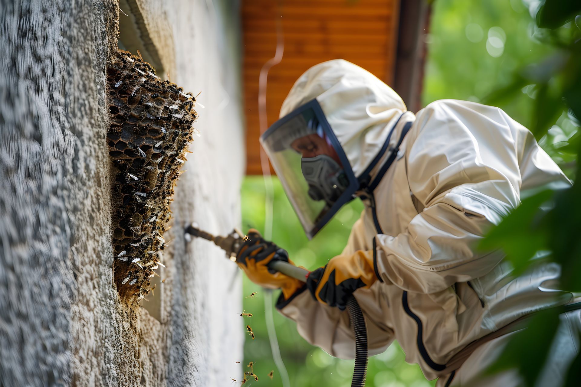Un technicien en désinsectisation, vêtu d'une combinaison de protection, pulvérise un nid de guêpes sur un bâtiment.