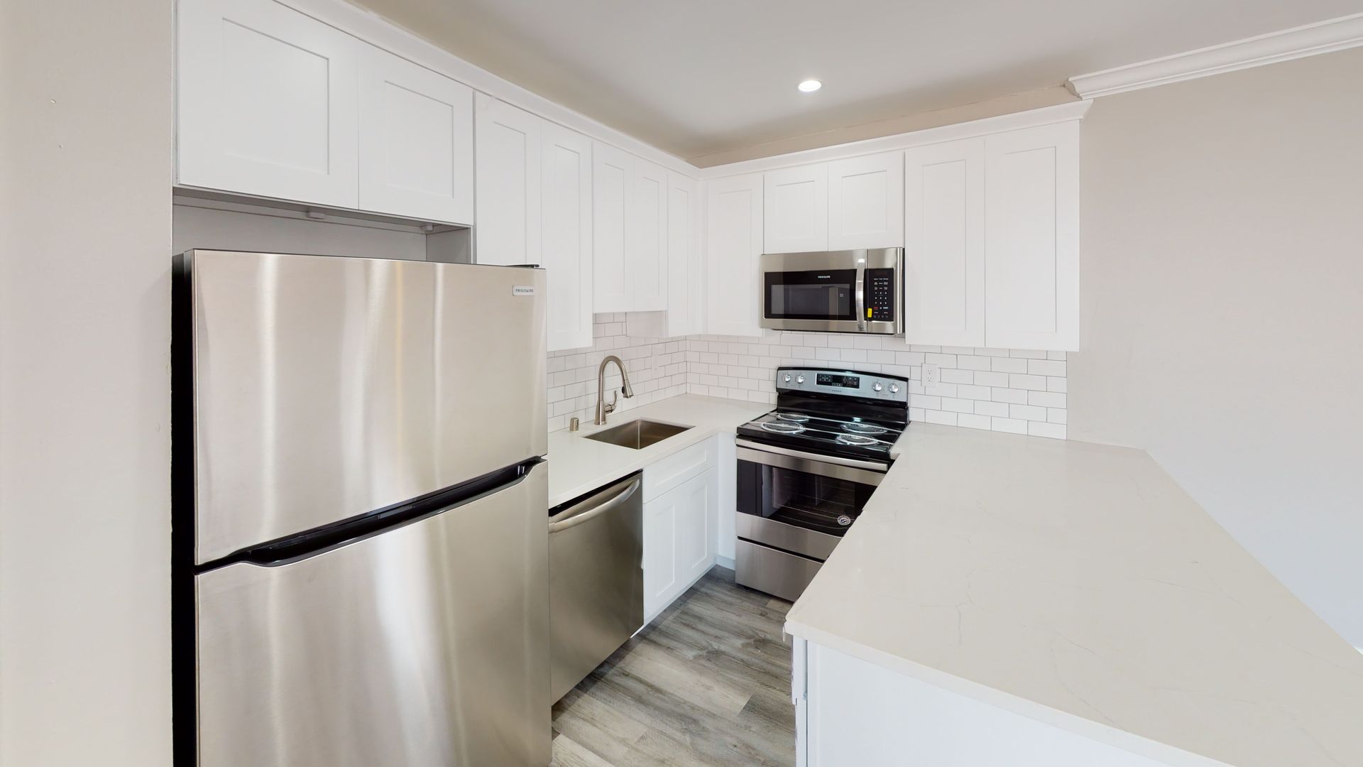 White kitchen with stainless steel appliances, white cabinets, and white countertops.